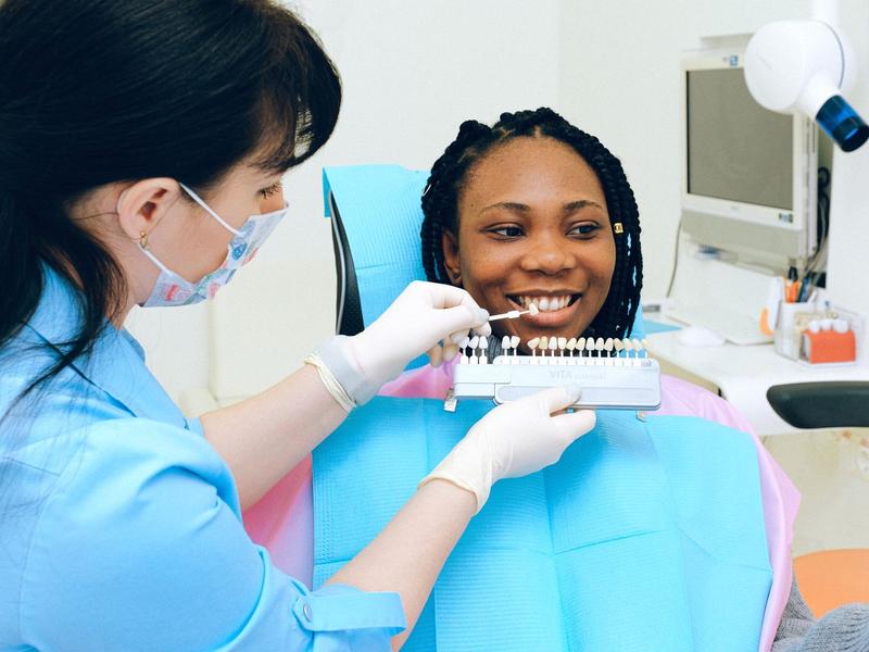 Smiling patient in a dental chair while a dental professional compares tooth shades