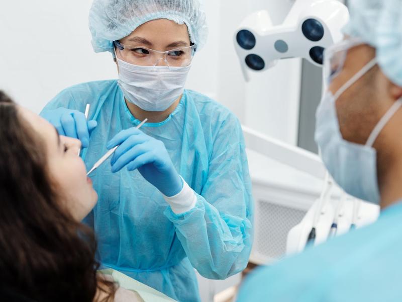 Dentist and assistant in blue gowns treating a patient's tooth