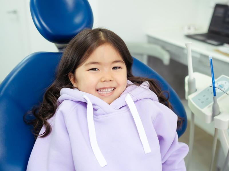 Smiling child in a purple hoodie sitting in a blue dental chair