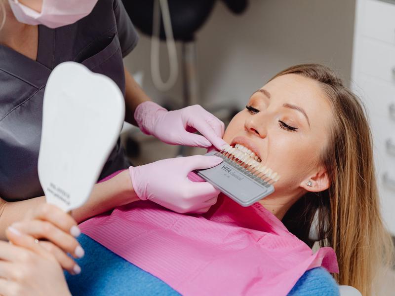 Dental professional holding a tooth shade guide next to a smiling patient