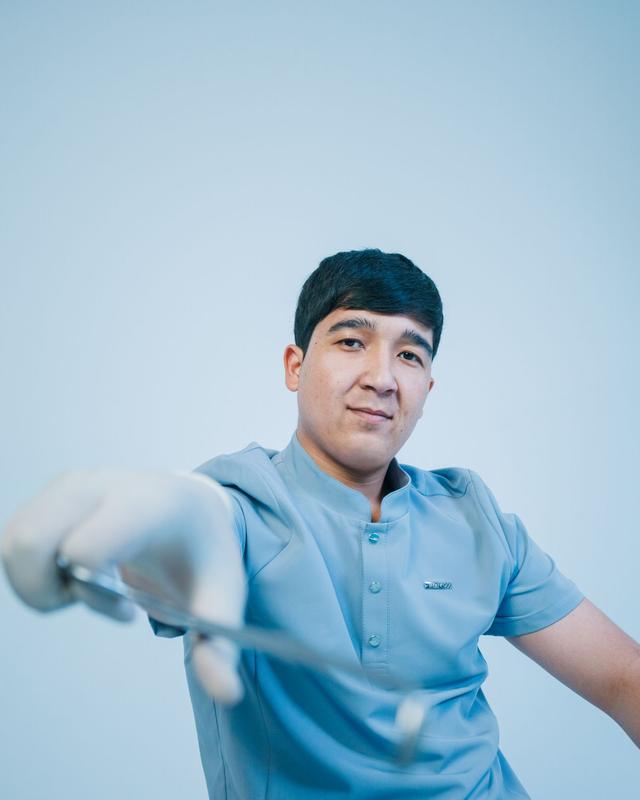 Friendly dentist in light blue scrubs holding a dental instrument