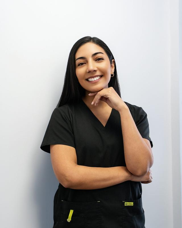 Smiling dental professional in black scrubs standing against a white wall