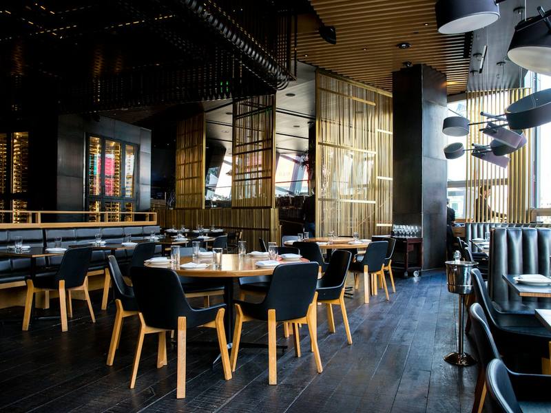 Warm, modern restaurant dining room with wooden tables and pendant lighting