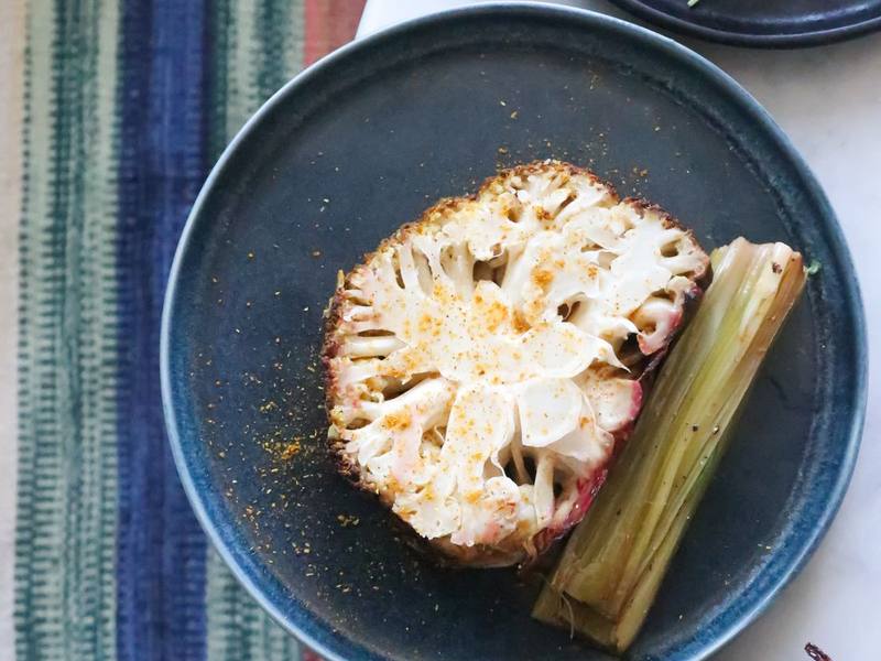 Roasted cauliflower steak on a dark plate with grilled vegetables