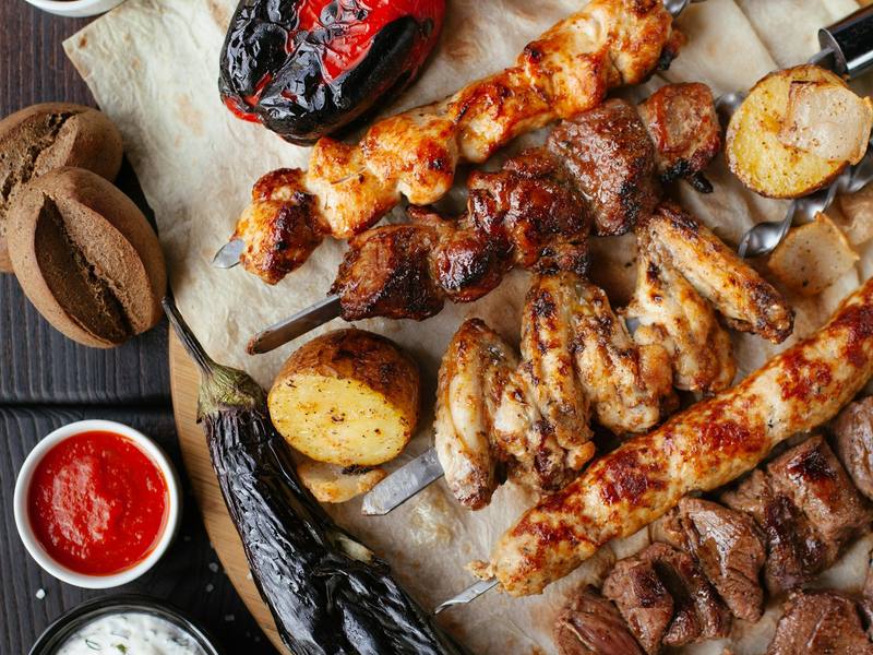 Grilled skewers and charred vegetables on a wooden board with dips