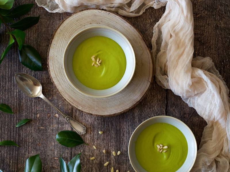 Bowls of smooth green pea soup surrounded by fresh herbs