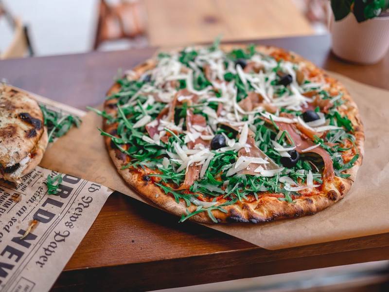 Wood-fired flatbread topped with prosciutto and fresh arugula