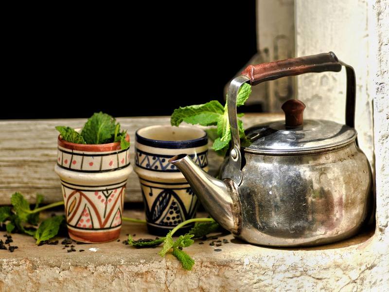 Metal teapot and cups of fresh mint tea with mint leaves on a wooden table