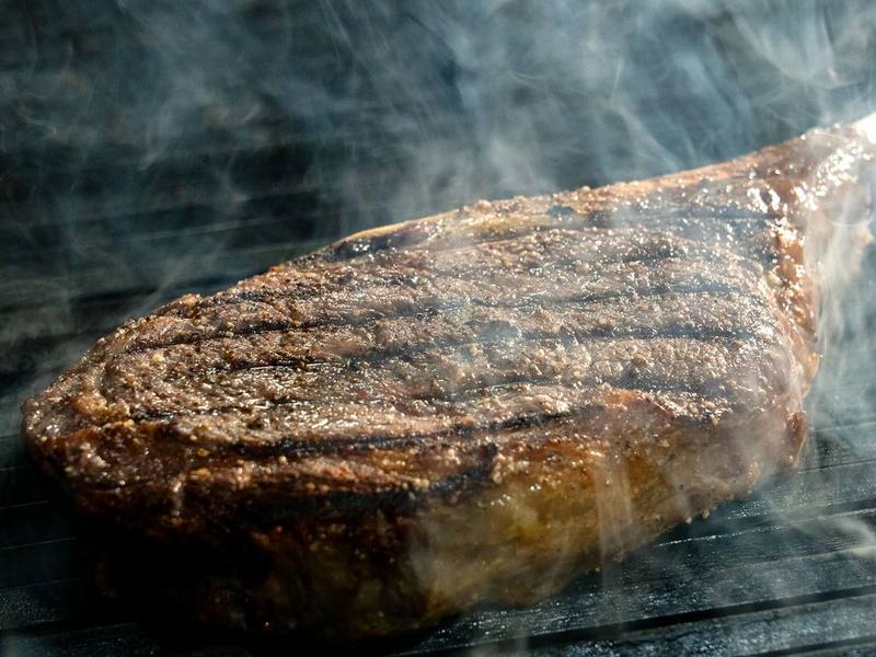 Bone-in ribeye steak with grill marks smoking on the grill