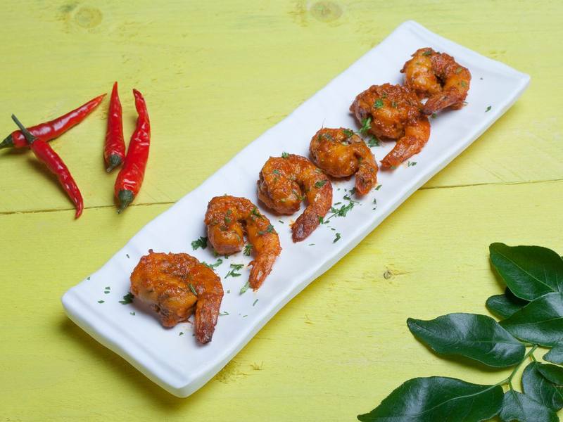 Spicy grilled shrimp with red chili peppers on a white platter
