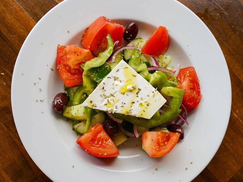 Greek salad with tomato, cucumber, olives and a slab of feta on a white plate