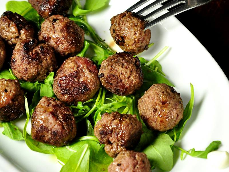 Spiced meatballs on a bed of fresh herbs and arugula on an oval plate
