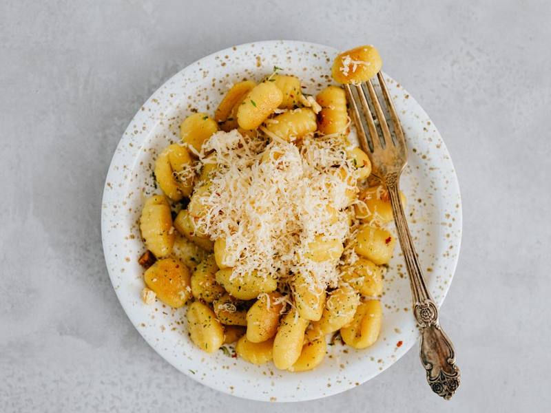 Golden gnocchi with grated cheese on a speckled plate with a fork