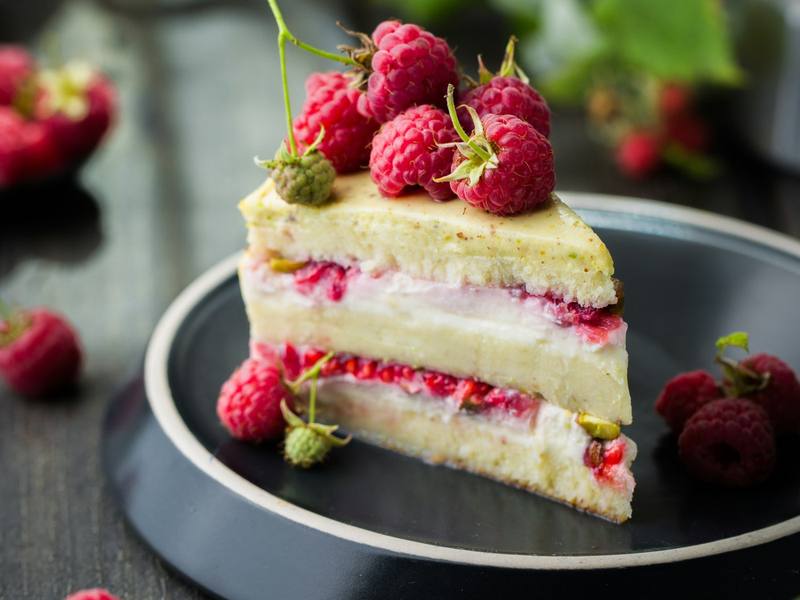 Slice of layered raspberry cake with fresh raspberries on a dark plate