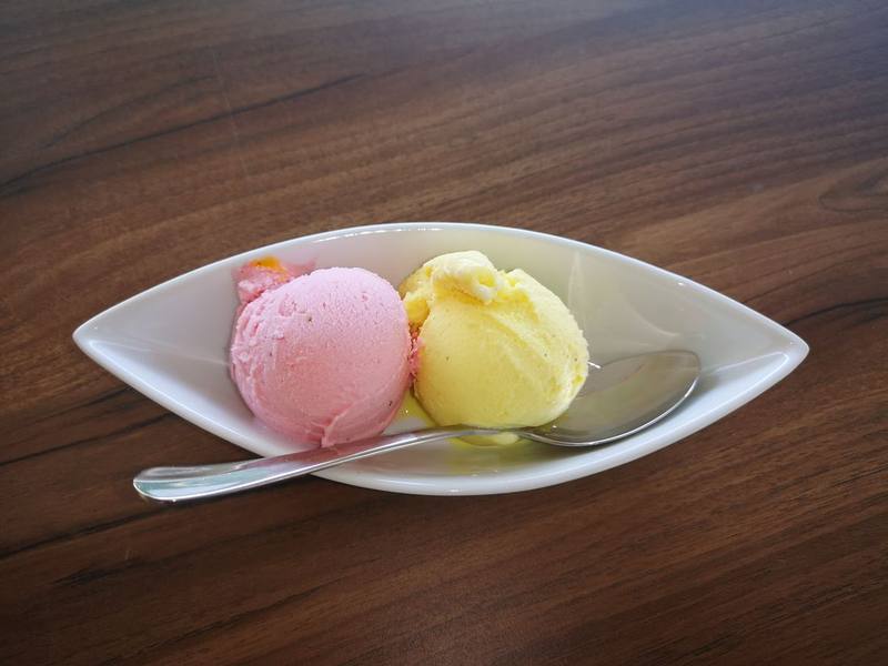 Scoops of pink and yellow sorbet in a white dish with a spoon