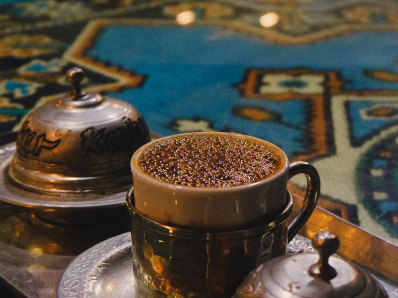 Turkish coffee in an ornate cup next to a traditional copper cezve