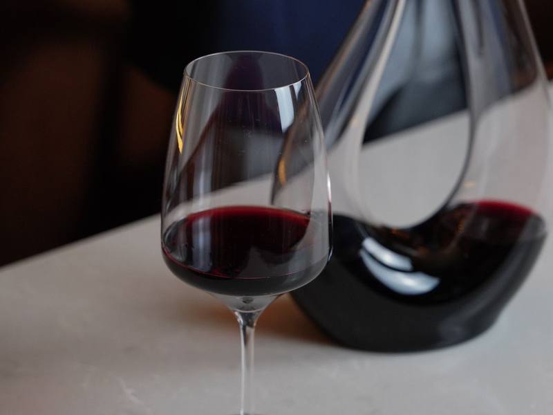 Glass of red wine beside a decanter on a white table