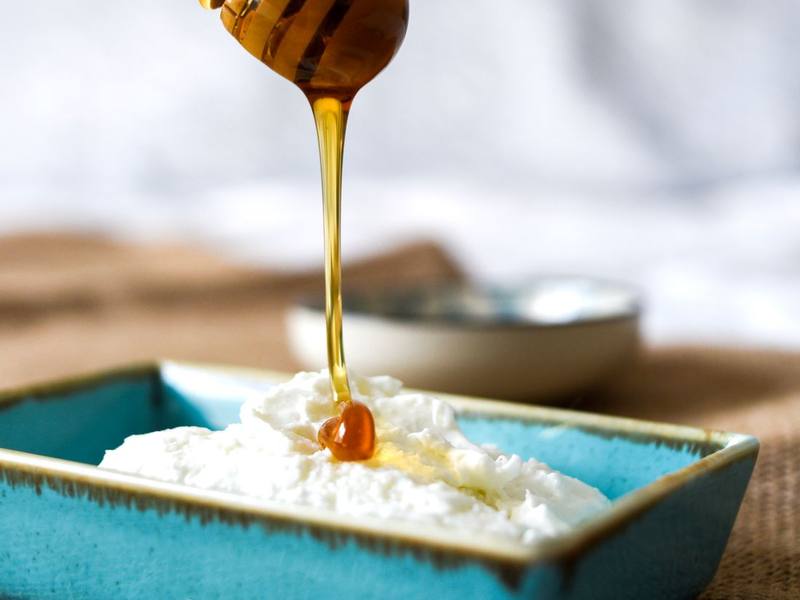 Honey drizzling from a wooden dipper onto creamy whipped cheese in a teal dish