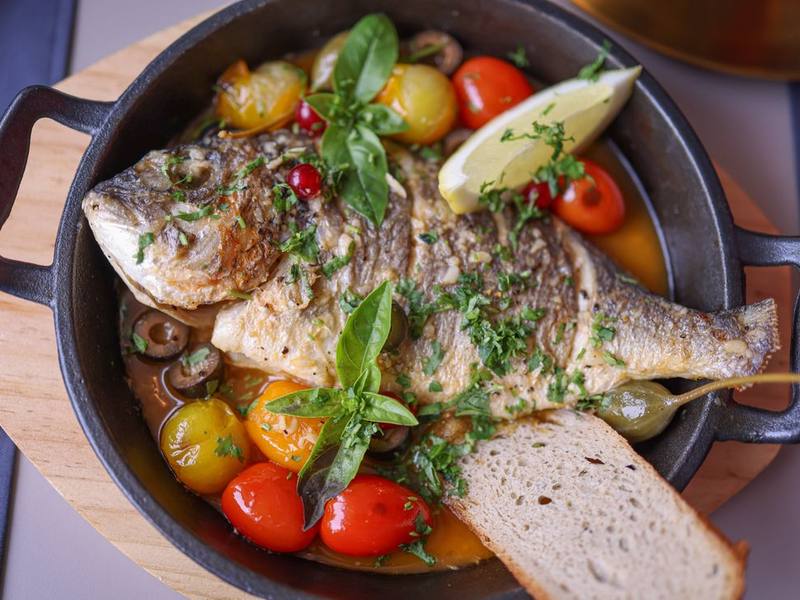 Whole roasted fish with cherry tomatoes, lemon and herbs in an iron pan