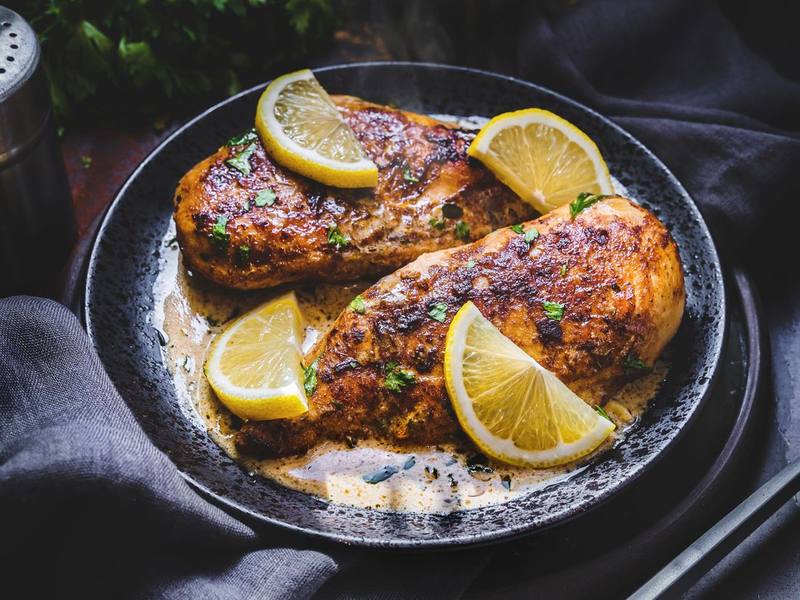 Roasted chicken pieces with lemon slices on a dark plate